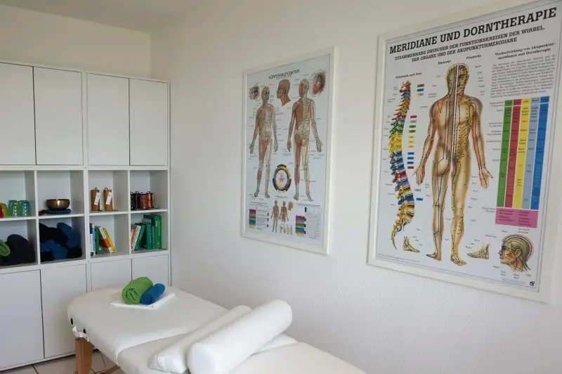 Behandlungsraum mit Liege und Lehrtafeln zu Meridianen und Dorntherapie